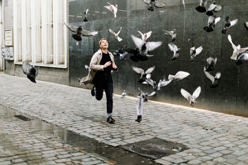 City pigeons taking flight as a happy girl runs quickly through them