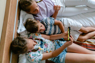 Obraz na płótnie Canvas Children lying in bed and watching a cartoon on the phone