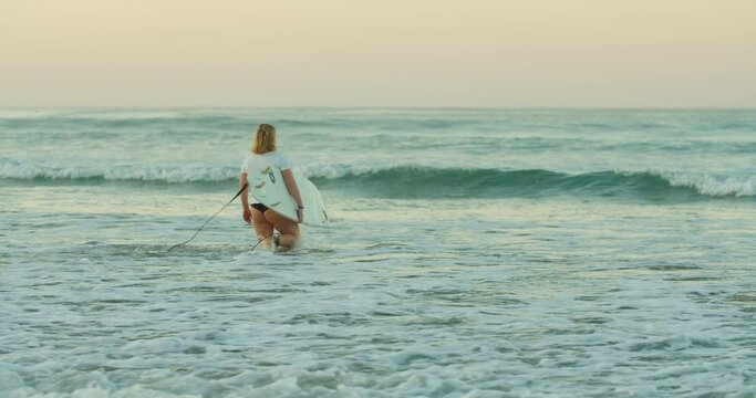 Female surfer with board walk in shallow Costa rica waves in sunrise; slide