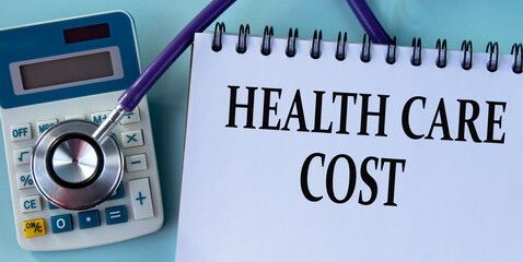 HEALTH CARE COST - words on a white sheet against the background of a stethoscope and a calculator.