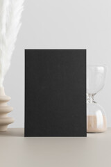 Black invitation card mockup with a pampas decoration on the beige table. 5x7 ratio, similar to A6, A5.