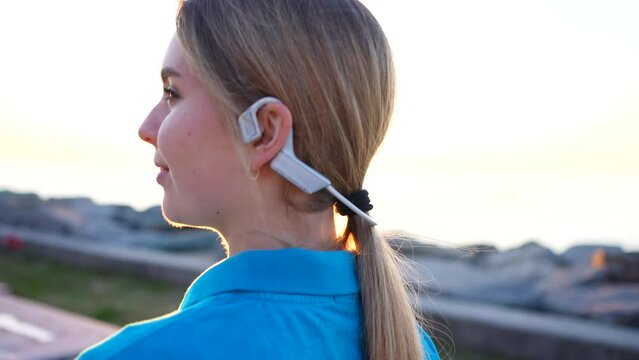 positive young woman in bone conduction headphones in sunset
