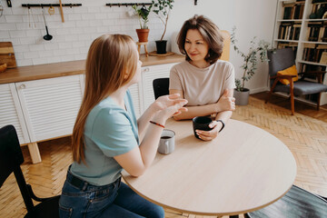 cute teenage girl and her charming beautiful middle aged mother talking in the kitchen