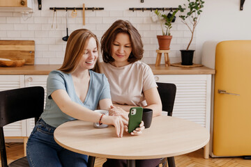 young daughter visits her charming middle-aged mother and shows her photos on her smartphone