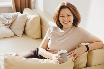 Woman sitting on the sofa in the living room with a mug of coffee