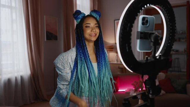 Cheerful African woman blogger with dreadlocks dances on camera phone at home