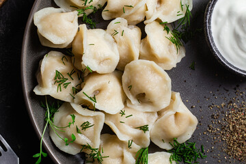 Dumplings with sour cream and herbs on a dark plate. Meat dumplings