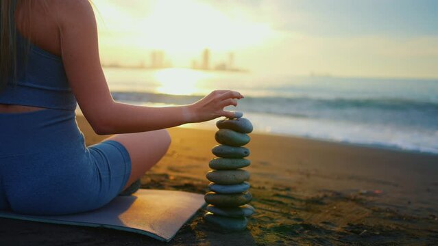 concept idea balance healthy lifestyle fitness yoga ,a woman builds a pyramid of stones ocean shore sunset close up Zen style