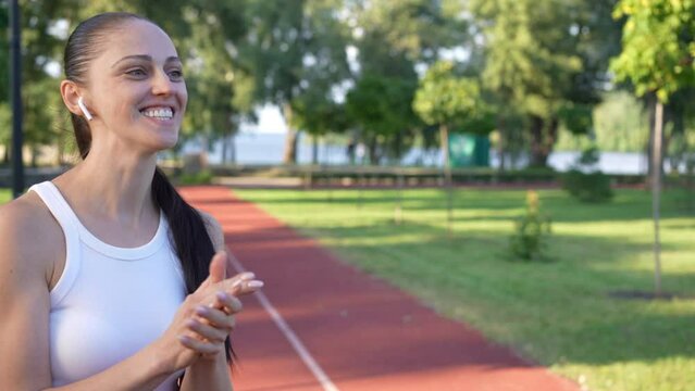 Joyful motivated young woman clapping endorsing friends training for marathon outdoors. Smiling positive Caucasian sportswoman supporting group of women jogging passing leaving - Powered by Adobe