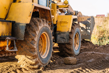 Fototapeta na wymiar A large yellow wheel loader aligns ground for a new building. Land preparation for the auction or sale. Plot leveling and adding sand for construction. Banner. Copy space. Special transport. Closeup