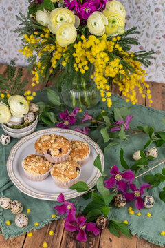 Tischdekoration im Frühling mit frischen Blumen und Muffins, Blumenstrauß und Gepäck auf einem Tisch