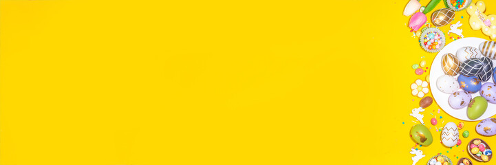 High-colored Easter baking background, Easter sale, party invitation flatlay, Colorful Easter eggs, chocolate eggs and bunny rabbit with sugar sprinkles on bright yellow background top view copy space