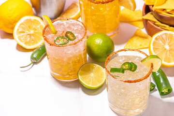 Set of tequila margarita mexican cocktails, with jalapeno pepper, lime and spicy rim, on high-colored tiled background copy space