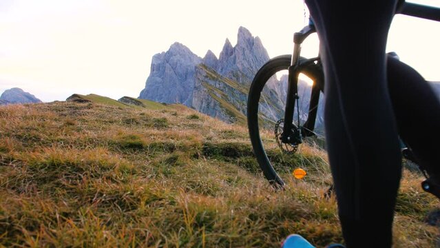 Young man with mountain bike walking on Seceda mountain peak at sunrise. Puez Odle, Trentino, Dolomites, Italy.
