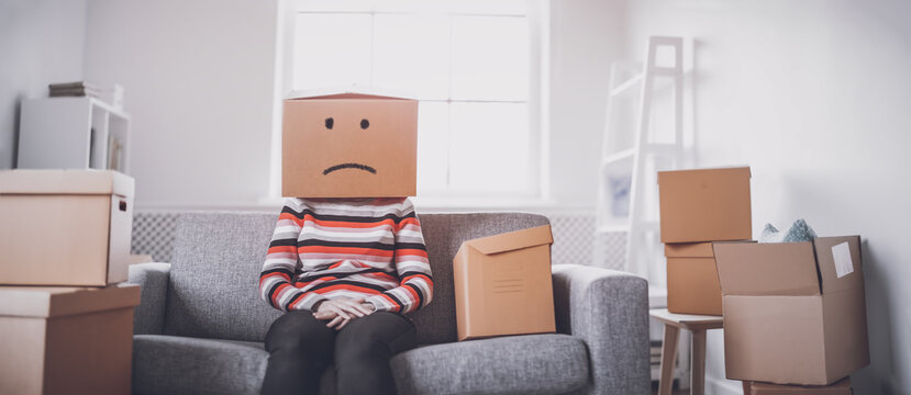 Tired Sad Woman With Cardboard Box On Her Head Sitting On The Sofa In Her New House.