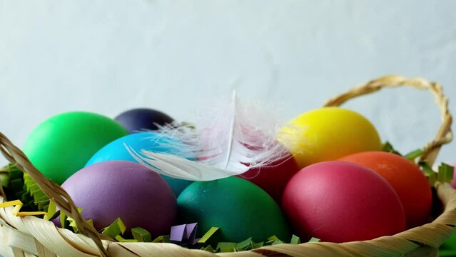 White feather falls on a basket of colored Easter eggs side view closeup