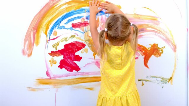 small child, blonde girl in yellow dress paints rainbow with her hands orange paint on white wall, childish naive drawing, acrylic, happiness childhood, creative development, Masterpiece artwork