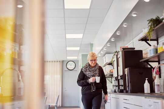 Mature woman having coffee break in office kitchen