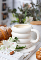 A cup of aromatic cappuccino and a croissant on a white tray