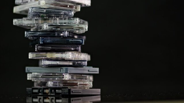 A stack of audio cassettes spins on a black background and mirror surface. Golden nineties.