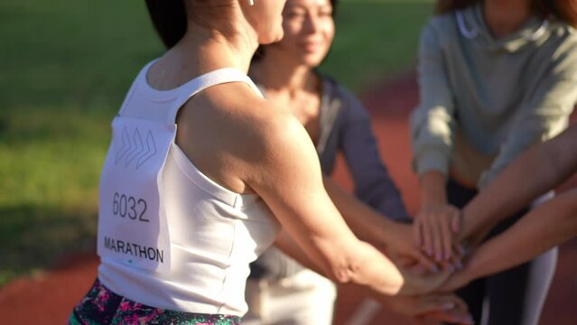 Group of unrecognizable young sportswomen stacking hands gesturing in slow motion before marathon. Motivated confident young fit Caucasian women rejoicing participation in charity run in sunshine