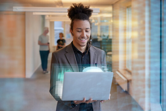 Young businessman holding laptop in office corridor