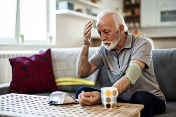 Senior checking his blood pressure. Senior man examining blood pressure in bedroom at home during the day.