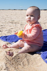 Baby girl playing in the sand with plastic toy. 8 months old baby with blonde hair at the beach.