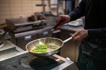 man chef cooking fried green bean in frying pan on restaurant kitchen
