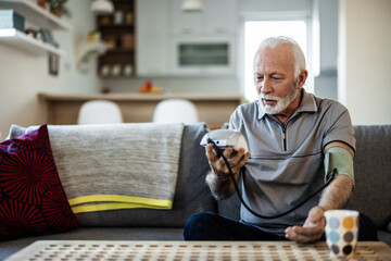 Caucasian man taking his own blood pressure. Active senior man measuring blood pressure with sphygmomanometer in living room.