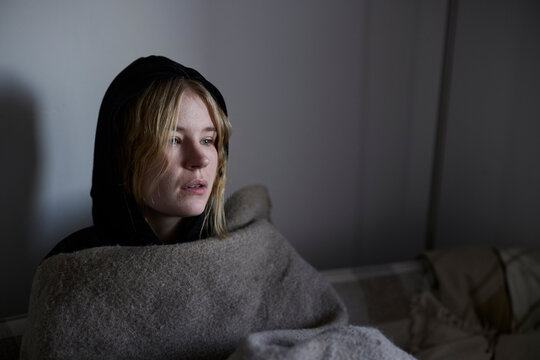 Teenage girl sitting on sofa wrapped in blanket