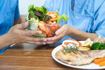 Asian elderly woman patient eating Salmon steak breakfast with vegetable healthy food while sitting and hungry on bed in hospital.