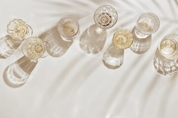 Flat lay with white sparkling wine bottle, set glasses wine with sunshine shadow and flare on light...