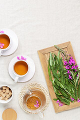 Herbal tea from kipreya leaves in white cups on linen fabric table background, fireweed green leaves and flowers on wooden tray. Flavored herbal tea from wild plants, healing hot beverage.