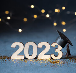 Class of 2023 concept. Wooden number 2023 with graduate cap on dark background with bokeh