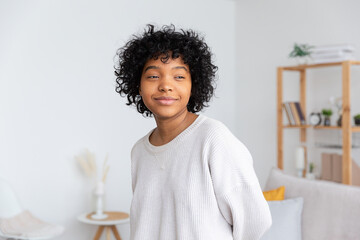 Beautiful african american girl with afro hairstyle at home indoor. Young african woman with curly hair in living room. Beauty ethnic people, domestic life concept.
