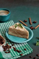 Fresh delicious Cake Napoleon with cream on a green background. A cup of hot coffee, cinnamon stick, badyan, coffee beans on a green background. Copy space