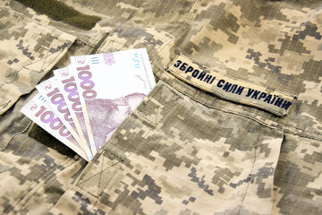 Ukrainian UAH banknotes against the background of a military pixel, the uniform of the military forces of Ukraine.