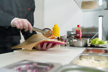 Cook preparing traditional Greek pita souvlaki dish with grilled meat, Korean carrot and vegetables