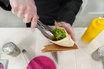 Cook stuffing pita souvlaki with fresh salad leaves and marinated chicken meat. Chef cooks traditional Greek fast food in a restaurant kitchen, shot from above