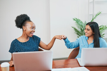 Two women give fist bump over conference table, diversity celebrated