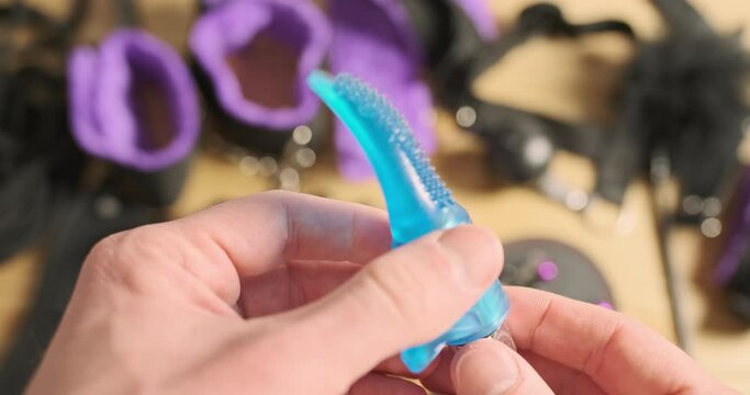 Men's hands turn on small vibrator, checking its work. In the background, on table a lot of sex toys for bdsm.