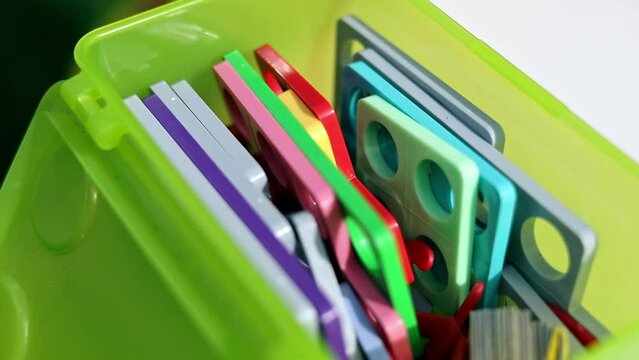 The Numicon shapes close-up when autistic child is having therapy maths lesson, counting with the help of Numicon shapes, writing results on the paper, sitting by the white table outside on the garden