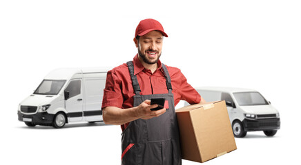 Male logistic worker typing on a mobile phone and holding a cardboard box in front of vans