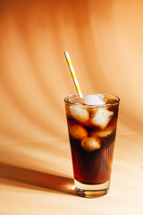 close-up on a glass with cola and ice on a beige background with shadows