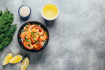 top view of a dish of rice and shrimp in a plate next to sauce herbs and butter on a grey background with free space for text