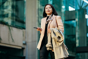 Smiling Asian businesswoman walks on street.