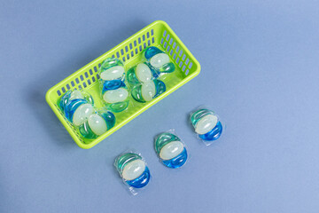 Gel for washing in capsules in green plastic basket. Organization of storage in the laundry or at...