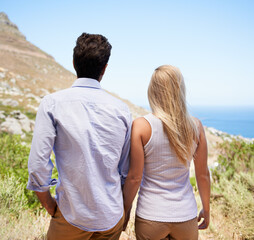 Admiring the beautiful view. Rear view of a young couple standing hand in hand on the slope of a mountain.