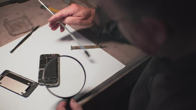 an adult man in the workshop disassembles a smartphone to find out the cause of the breakdown. the master uses a magnifying loupe.close-up. High-quality shooting in 4k format